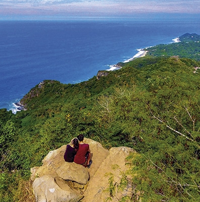 Young couple on a rocky hilltop with a view of the Pacific Ocean in Riviera Nayarit MX